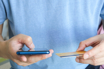 Young man sat in the living room on sofa , using his phone, a smartphone and holding credit card her online To buy product in the internet