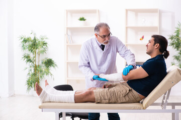 Fototapeta premium Young injured man visiting old doctor traumatologist