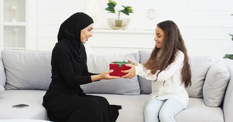 Daughter coming to muslim mother in hijab with present behind back. Arabian woman in Abaya dress...
