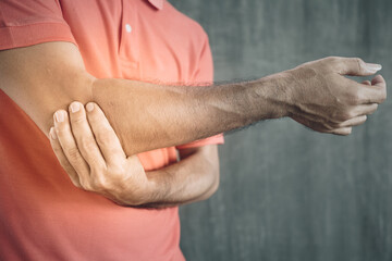 young man having elbow pain at arm on Cement wall background , Problems and health care concepts