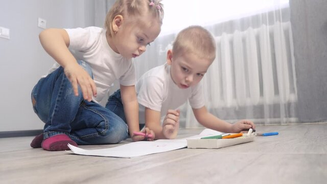 happy family brother and lifestyle sister teamwork concept. little boy and girl draw on the floor in a sketchbook. brother and sister in the room draw with crayons