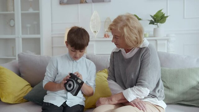 Adorable teen child using photo camera showing to his grandmother taking cute portrait pictures in the living room. Families. Entertainment. Photoshoot.