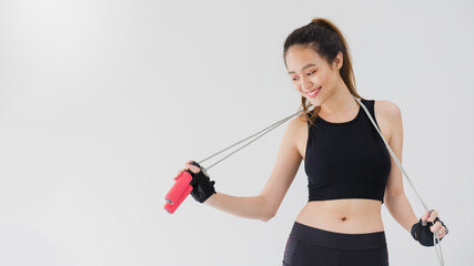 Asian beautiful smiling women exercise with jumping rope on white wall fitness background.Exercise for lose weight, increase flexibility and tighten the shape.Healthy lifestyle concept.