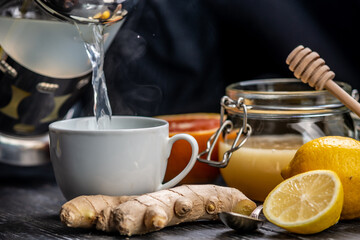 Person is pouring in a cup of vitamin warming tea with ginger, lemon and honey. Concept of useful and tasty tea in the cold days or with the flu