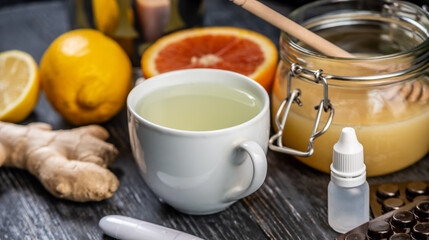 Fototapeta na wymiar Hot tea with ginger, honey, lemon and preparations for cold and a thermometer. Concept of vitamin healthy tea for the sick