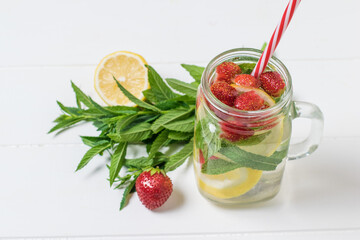 A mug of cold water with berries and lemon on a white table.