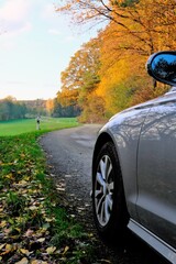 Car on the autumn road. Autumn travel and trips.Road view. Silver color car on the road  with trees with yellow foliage and green fields in the sunshine.Autumn landscape. Fall season