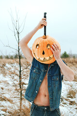 man in a denim jacket wearing a naked body with a Halloween pumpkin on his head, celebrating Halloween. a man with a knife in a Halloween costume cuts a pumpkin on his head