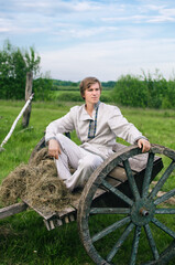 young man in national costume is sitting in an old cart in a field