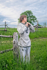 young man in national costume stands near an old wooden fence in a fiel