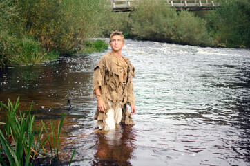 man in rags stands in shallow water in the river