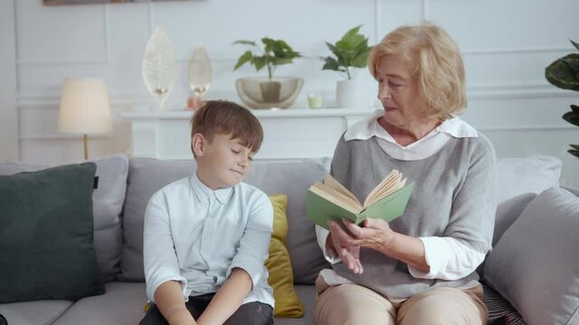 Tricky schoolboy doing homework with granma pretending to be tired. Generous old happy grandmother giving kid mobile phone. Upbringing. Funny scene.