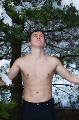 young man without a shirt in the winter forest sprinkles snow