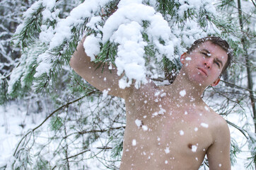 young man without a shirt in the winter forest sprinkles snow