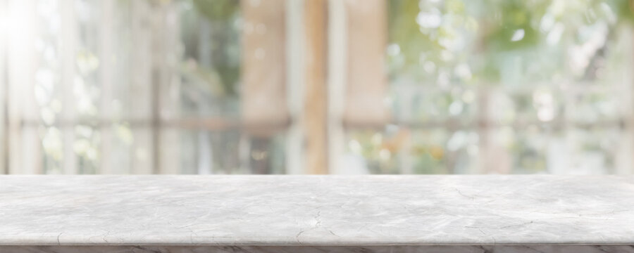 Fototapeta Empty white stone marble table top and blurred of interior restaurant with window view green from tree garden background background - can used for display or montage your products.