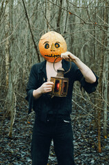 man in ragged clothes with a lantern and a Halloween mask on his head in a damp and gloomy forest on earth. pumpkin Jack