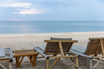 Bamboo deck chairs for tourists at peaceful beach under blue sky with calm sea morning light reflection as background. Picnic corner for visitors next to sandy beach