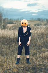 boy in rags and a pumpkin mask is standing in a field, possibly a Halloween maniac
