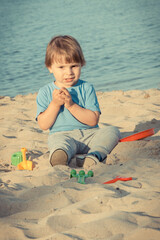 Happy boy sitting on beach and playing with sand. Vacation time concept
