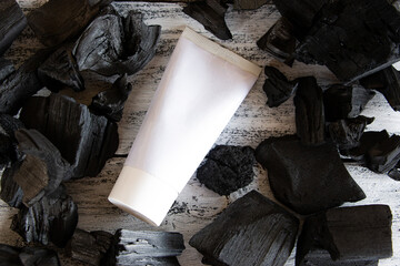 White cosmetic tube and natural black charcoal. Skin care concept. Creative layout with copy space.