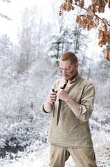 young soldier with bruises on his face stands in the winter forest with a knife in his hands