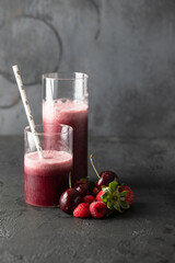 Two glasses with fresh berries smoothie and cherry, strawberry and raspberry fruit on dark background. Perfect drink for vegan and vegetarian diet