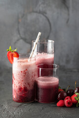 Different type glass with fresh berries smoothie and cherry, strawberry and raspberry fruit on dark background. Perfect drink for vegan and vegetarian diet