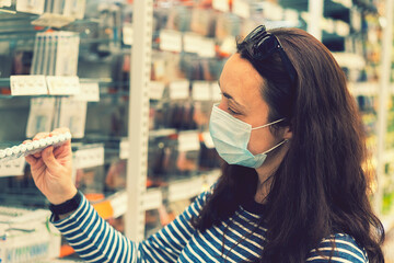 Woman in medical mask choosing goods in a store. Concept of shopping during quarantine at covid-19...
