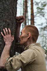young soldier with mud and bruises on his face leaned against the trunk of a pine tree in the winter forest
