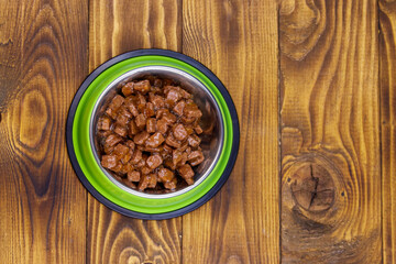 Canned food for cats or dogs in green metal bowl on wooden floor. Top view
