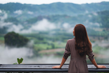 Rear view image of a female traveler looking at a beautiful foggy mountain and nature view