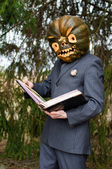 man in a business suit with a Halloween pumpkin on his head reads an old book