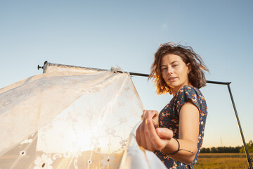A romantic walk of a curly-haired woman in a dress against the background of the a rack with white...