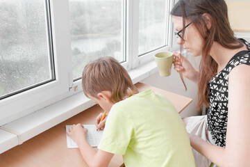 Boy learns to write letters sitting by the table. Doing homework with his mom