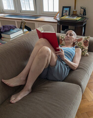 bald woman laying on sofa reading a book