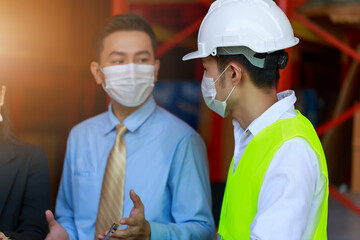 Asian businessman wearing protective face mask talking to engineer at the warehouse factory, new normal working after pandemic crisis.