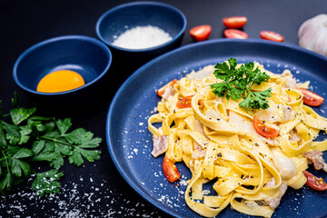 close up view of Pasta Carbonara. fettuccine with bacon, parsley, and parmesan cheese. Pasta Carbonara on blue plate with parmesan and garlic on dark background. Italian food concept.