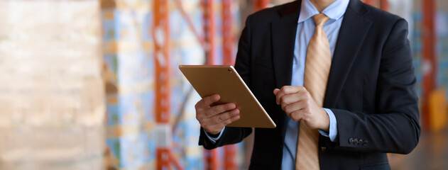 Close up businessman in black suit investor using tablet checking inventory in warehouse industry,...