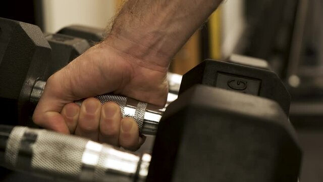 Dumbbells weights in a row. male athlete putting down dumbbells to weight rack, strength training equipment in gym. Muscle built body builder. Closeup

