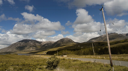 Irland: Zeitlos anmutende Landstraße führt an Hügeln unter Wolkenschatten entlang in ein Tal