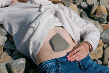 Stone on the girl's belly. Unrecognizable girl lying on a stone beach in the fall