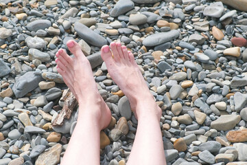 Women's feet in stones beach with pebble