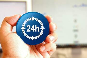 24 hours delivery icon blue round button holding by hand infront of workspace background