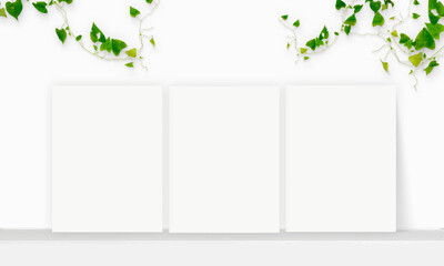 Three Interior vertical rectangular poster mockup standing on the table with plant and decorations on empty white wall background. Rendering illustration.