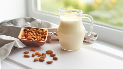 Almond milk in glass with almonds in wooden bowl on a white wooden table