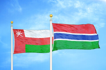 Oman and Gambia two flags on flagpoles and blue sky