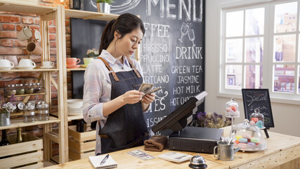Portrait of asian female businesswoman counting finances in small coffee shop. young girl waitress in apron standing in counter holding lots of money from cash box doing accounting after a day end.