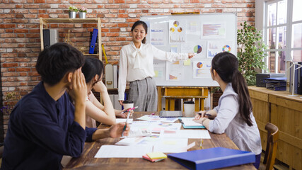 businesswoman at whiteboard giving presentation in modern boardroom. beautiful girl employee point at graph on flip chart and explaining opinion to male and female colleagues