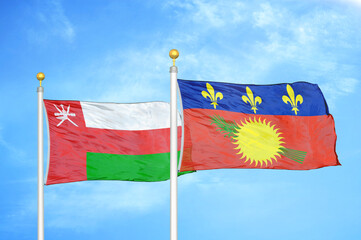 Oman and Guadeloupe two flags on flagpoles and blue sky