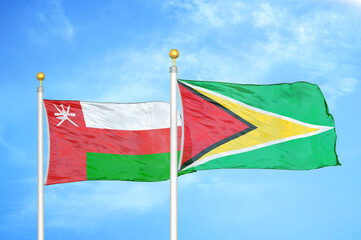 Oman and Guyana two flags on flagpoles and blue sky